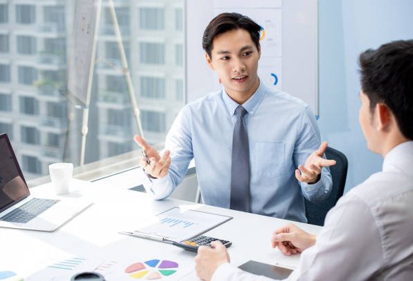 Attractive Asian financial broker explaning business data to his client during their private meeting in the office